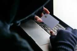 person in a hoodie and fingerless gloves holding a credit card over a laptop