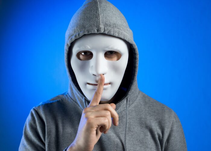 man in a hoodie and mask with finger over lips