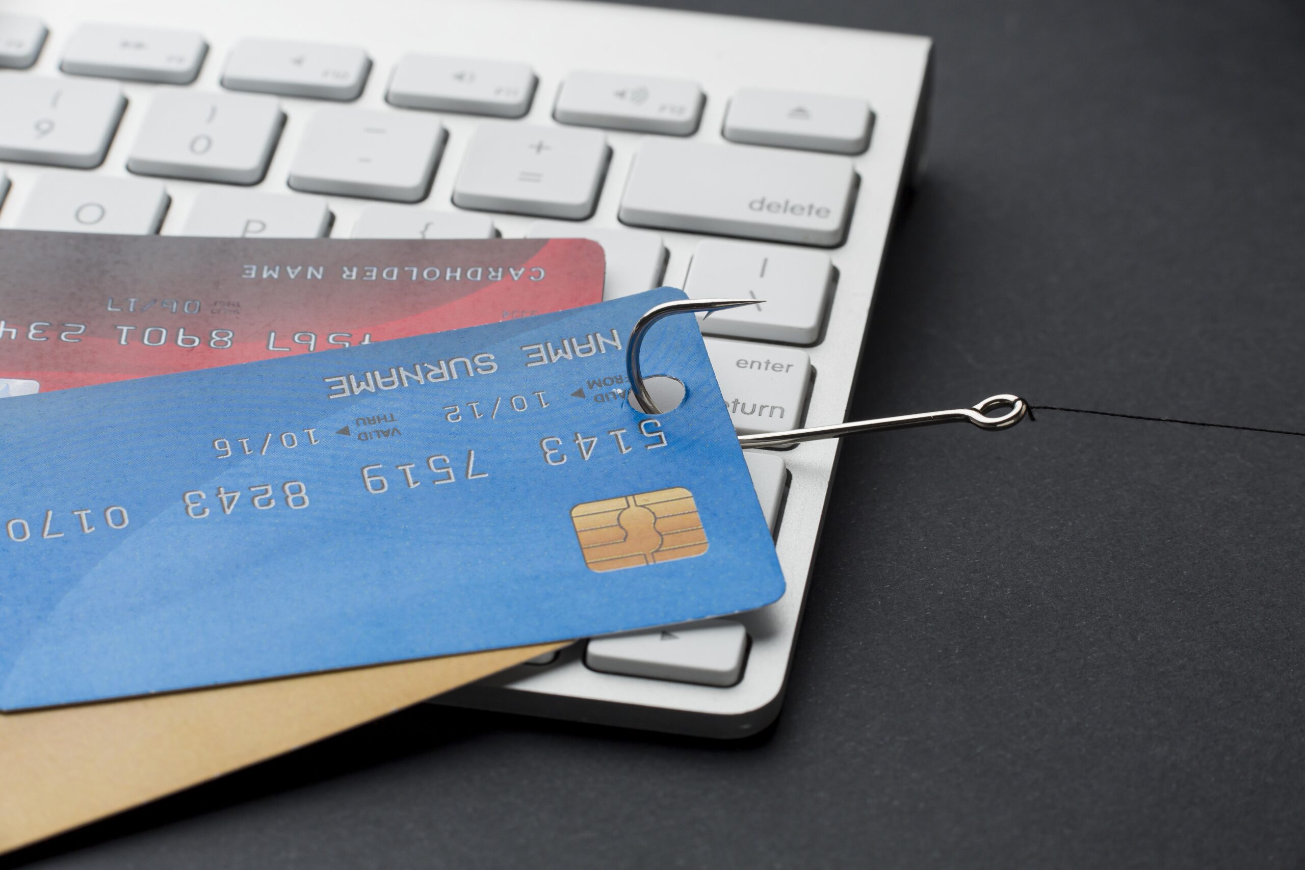 credit cards with a fish hook through them placed on top of a computer keyboard